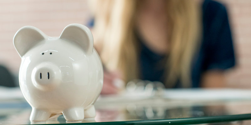 A high school teenager is writing down monthly budget in her notebook. A piggy bank is sitting on the table.